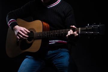 A man is playing an acoustic guitar while sitting