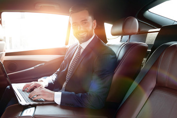smiling businessman sitting in the back seat of a prestigious ca