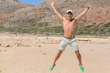 Horizontal portrait of a young man on vacation, happy jumping up on the beach. copy space