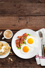 Fried eggs, bacon and italian ciabatta bread on white plate. Cup of coffee. Breakfast. Top view. Wooden background