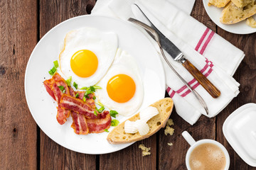 Fried eggs, bacon and italian ciabatta bread on white plate. Cup of coffee. Breakfast. Top view....