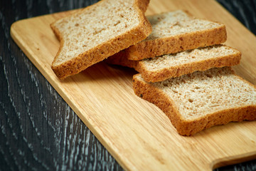 Sliced bread on wooden cutting Board, on dark wooden background, bran