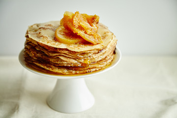 Crepes cake with orange jam and honey on white cake stand. Pancake breakfast concept