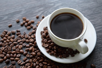 White Cup of black hot coffee with coffee beans on dark wood background