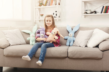Obraz premium Happy little female child hugging her toy rabbits on sofa at home