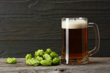 Glass beer with hop cones and wheat ears on dark wooden background with copy space. Beer brewery concept. Beer background
