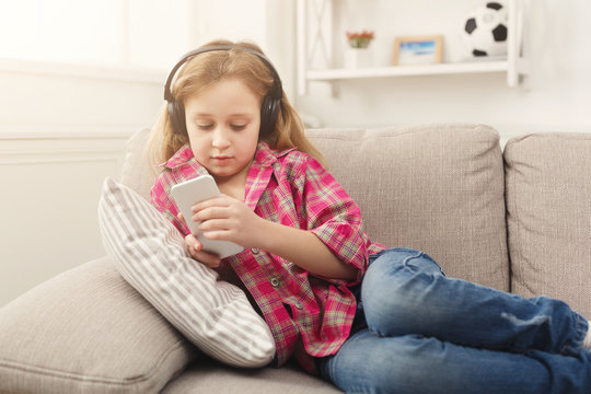 Happy little female child listening to music on sofa at home