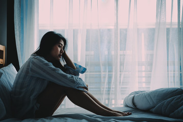 Asian woman sitting on a bed looking sad