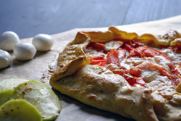 Homemade pizza with tomatoes, mozzarella cheese and zucchini on a wooden table.