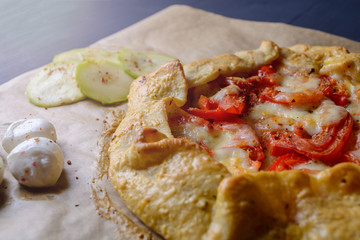 Homemade pizza with tomatoes, mozzarella cheese and zucchini on a wooden table.