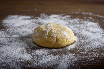 Raw dough ball sprinkled with white flour on a wooden table.