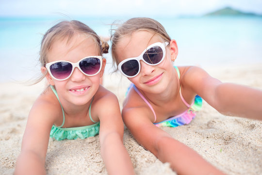 Close up little girls on sandy beach. Happy kids lying on warm white sandy beach