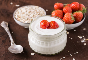 White yogurt in glass bowl with spoon and starwberries on rustic background.