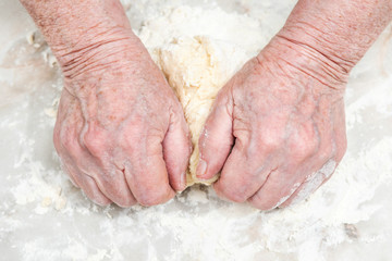 Female old hands knead the dough on a table, close-up