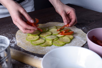 front view of the process of cooking vegetable biscuits, pizza. women's hands lay out red tomatoes on a rolled dough