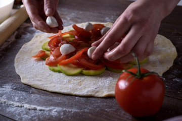 front view of the process of cooking vegetable biscuits, pizza. women's hands lay out mozzarella cheese on tomatoes and zucchini on a rolled dough