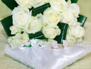 Obraz premium Wedding rings on a white satin wedding cushion against a bouquet of white roses
