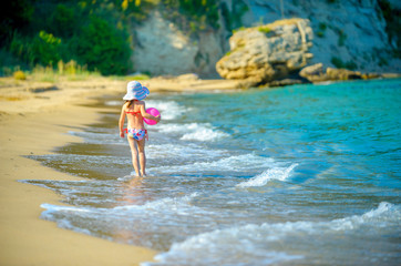 little girl in a hat with a sword in her hands walking along the seashore