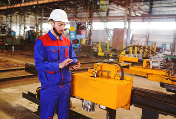 Portrait of a beautiful engineer in a construction helmet with a touch tablet on a factory background