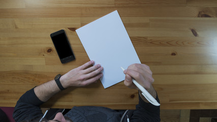 Man writing on blank white paper with smartphone near