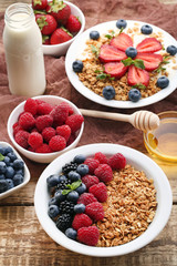 Granola with berries in plate, milk and honey on wooden table