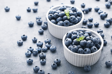 Ripe blueberries in bowls on grey wooden table