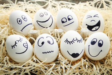 Eggs with funny faces in nest on wooden table