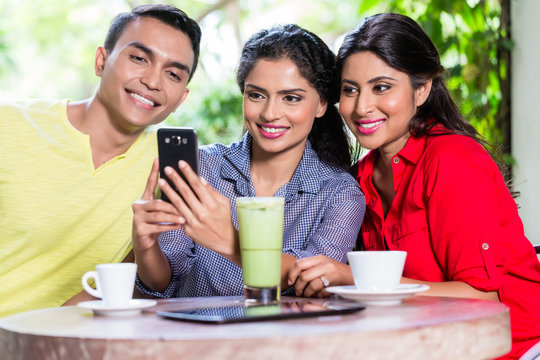 Indian girl showing pictures on smart phone to her friends in an Indian cafe