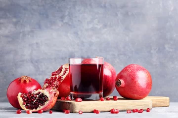 Photo sur Plexiglas Jus Pomegranate fruit and juice in glass on grey wooden table