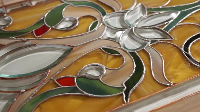 Graceful multi colored stained-glass is lying on a workplace of master. Camera is moving over it and showing all surface