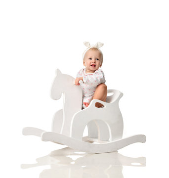 Toddler baby girl is riding swinging on a rocking chair toy horse over white 