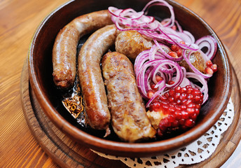 appetizing fried sausages in a frying pan with blue onion rings and pomegranate seeds. Georgian or Caucasian kitchen
