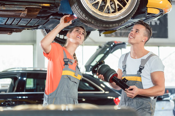 Experienced female auto mechanic checking tires before installing together with her colleague a new air suspension system in a modern automobile repair shop