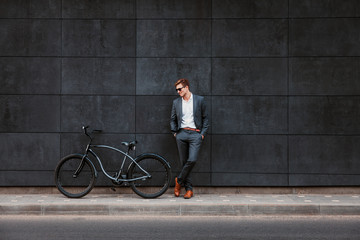 Fototapeta na wymiar Stylish young businessman in sunglasses stands near a bicycle