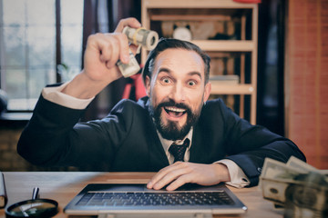smiling businessman sitting on laptop and demonstrating money on camera.