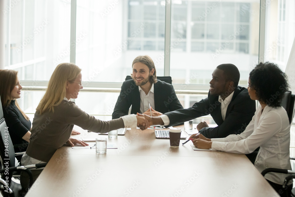 Sticker african businessman and caucasian businesswoman shaking hands over conference table at multiracial g