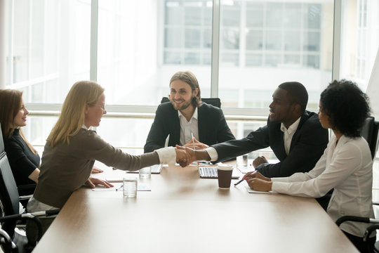 African businessman and caucasian businesswoman shaking hands over conference table at multiracial group meeting, diverse business team members handshaking starting collaboration, welcome new partner