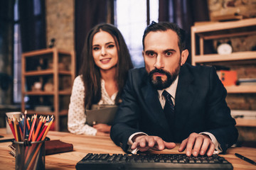 Beardy businessman attentively working on computer. Female paartner behind him.