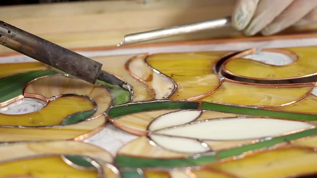 Skilled workman is covering frame of stained-glass by tin solder. Expensive technology of producing using copper tape and manual labour