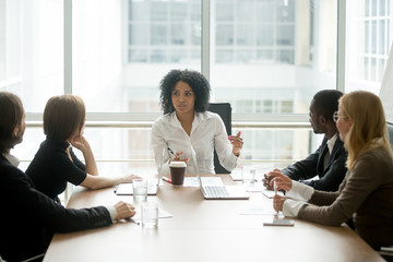 Black female boss leading corporate multiracial team meeting talking to diverse businesspeople,...