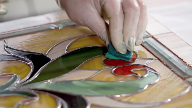 Close-up of masters hands are washing stained-glass. Panel is lying on a table, worker is rubbing a surface of product