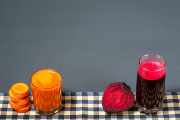 Natural juices from carrots and beets. The juice stands on a tablecloth, next to sliced carrots and beets. Tasty and healthy juice.