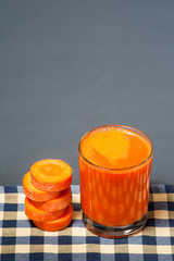Natural juice from carrots. The juice is poured into a clear glass, which stands on a tablecloth, next to sliced carrots.