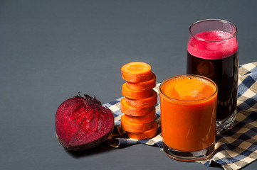 Natural juices from carrots and beets. Tasty and healthy juice is poured into a clear glass, next to sliced carrots and beets.