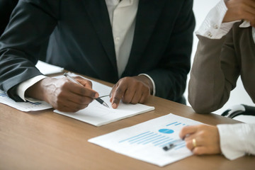 Diverse businessman and businesswoman working together with statistics, african man drawing graph explaining new idea for business improvement to caucasian colleague, project team teamwork concept