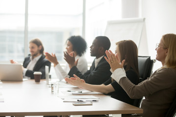 Multiracial business people applauding sitting at conference table, diverse team clapping hands...