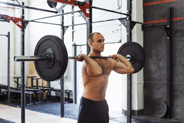 Fototapeta na wymiar Shot of muscular young man doing squats with barbell in a gym