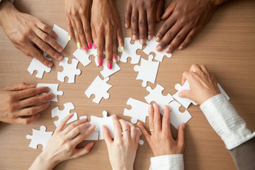 Hands of diverse people assembling jigsaw puzzle, african and caucasian team put pieces together searching for right match, help support in teamwork to find common solution concept, top close up view - obrazy, fototapety, plakaty