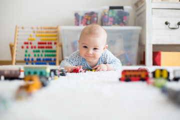 Cute little baby boy, playing with toy cars on the carpet in children room © Tomsickova