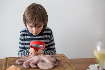 Fototapeta na wymiar Cute preschool child, boy, analyzing raw octopus with magnifying glass